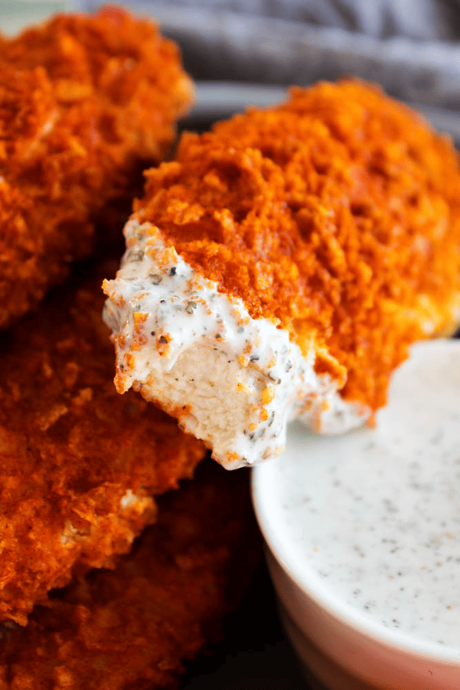 Baked buffalo chicken tenders on a plate. One has dip and a bite taken out