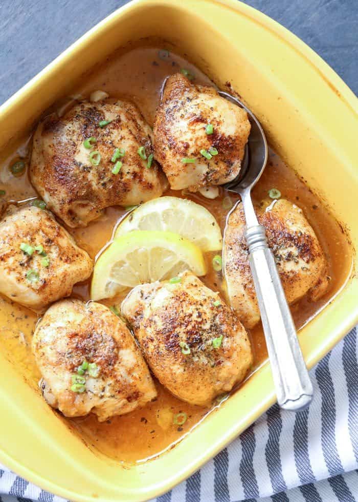 Baked lemon butter chicken thighs in a yellow casserole dish with lemon slices and a spoon