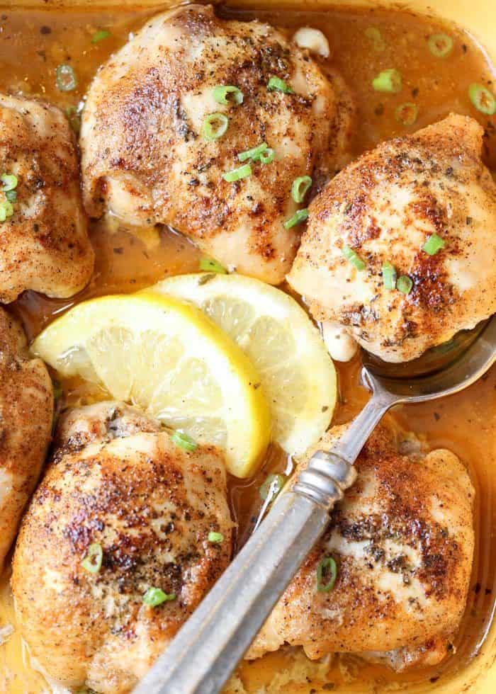 Baked lemon butter chicken thighs in a dish with lemon slices and a spoon