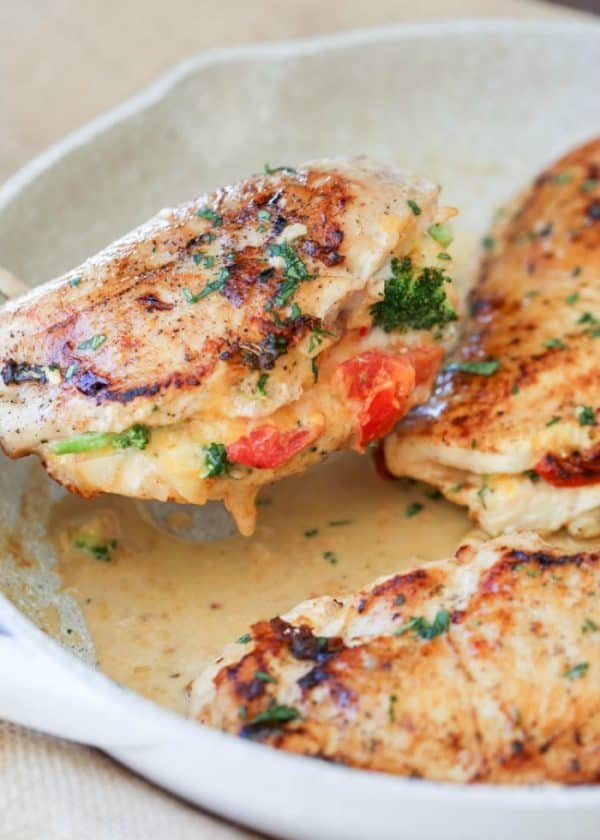 Broccoli tomato stuffed chicken breast in a casserole dish garnished with parsley