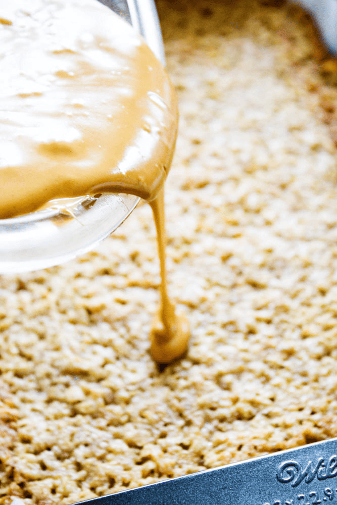 Butterscotch bars in a pan with peanut butter being poured on