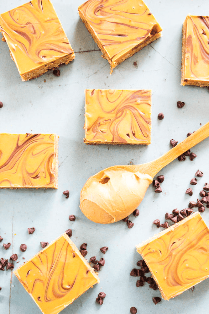 Butterscotch bars with peanut butter and chocolate chips on a marble board with a wooden spoon