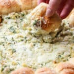Pull-A-Part crescents with spinach artichoke dip in a skillet with a piece of bread being dipped into the spinach dip