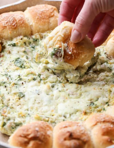 Pull-A-Part crescents with spinach artichoke dip in a skillet with a piece of bread being dipped into the spinach dip