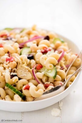 Mediterranean pasta salad in a white bowl with serving spoons