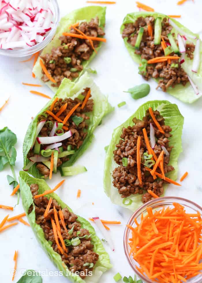 Chicken lettuce wraps on a marble board with carrots and radishes in bowls on the side