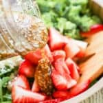 Spinach salad ingredients in a wooden bowl with dressing being poured on