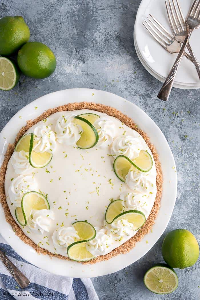 Key lime pie in a pie plate with forks and plates on the side
