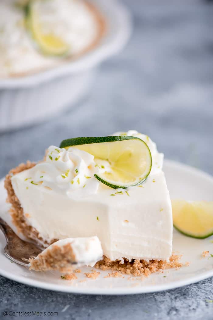 Piece of key lime pie on a plate with a bite on a fork