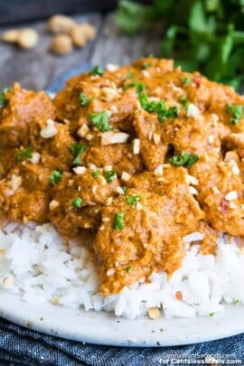 Butter chicken on a white plate with rice garnished with parsley and cashews