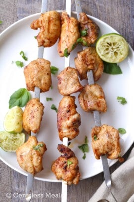 Lime grilled chicken kabobs on a white plate with cilantro and lime wedges
