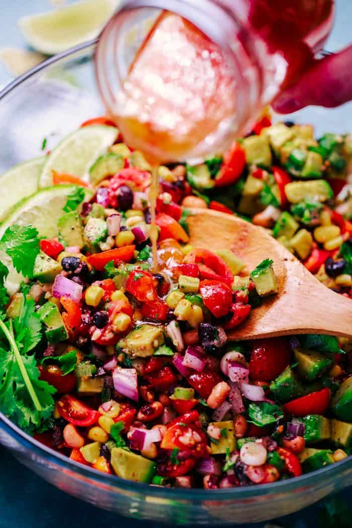 Texas caviar in a bowl with a spoon with dressing being poured on