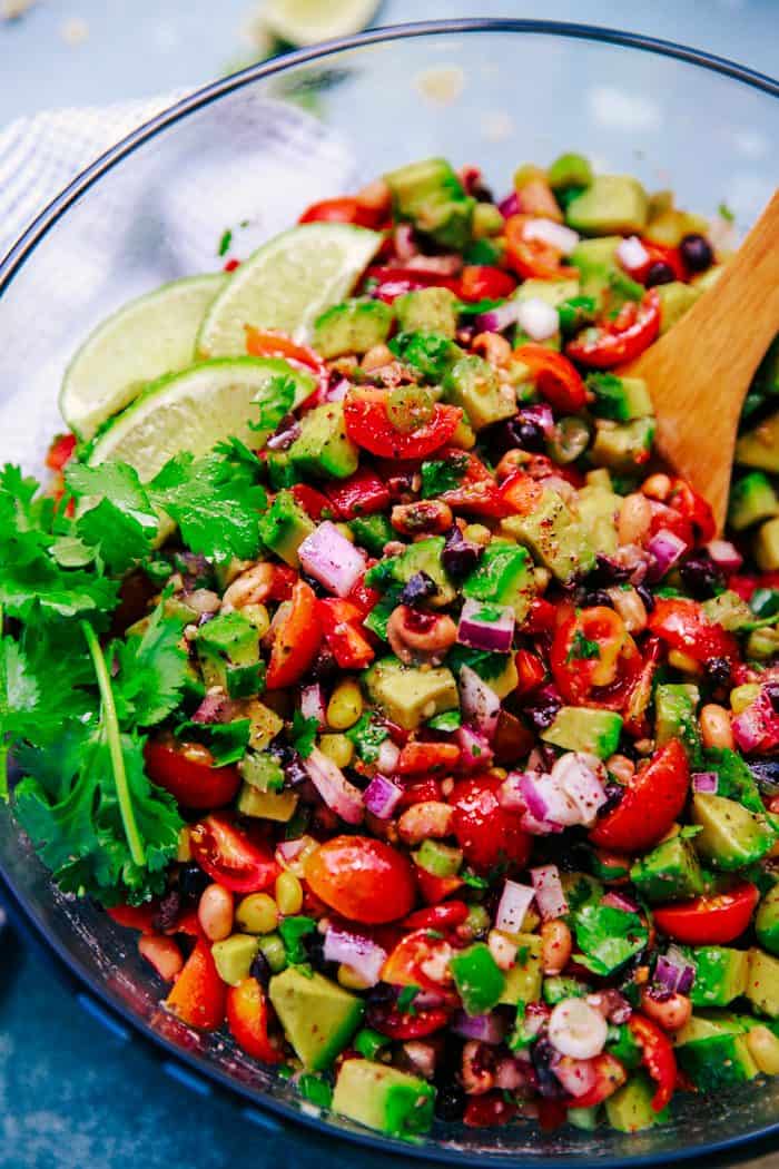 Texas caviar in a glass bowl with cilantro and lime wedges