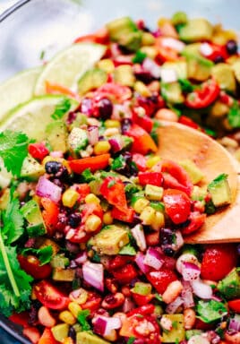 Texas caviar in a bowl with a wooden spoon garnished with cilantro and lime wedges