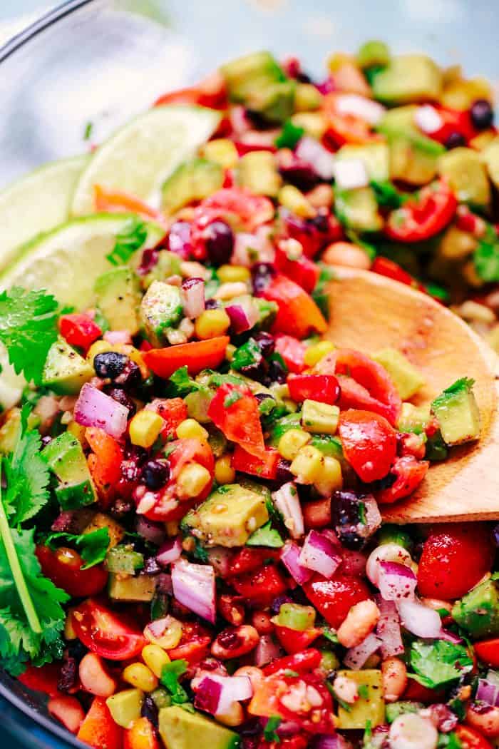 Texas caviar in a bowl with a wooden spoon garnished with cilantro and lime wedges