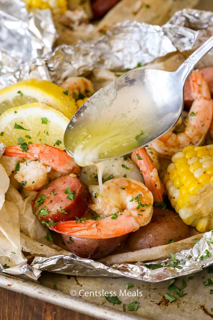 Butter being poured on shrimp boil foil packets