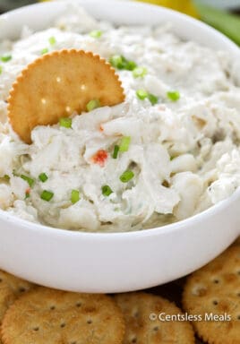 Crab dip in a white bowl garnished with green onions with a cracker
