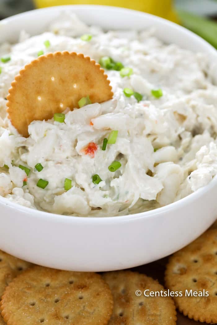 Crab dip in a white bowl garnished with green onions with a cracker