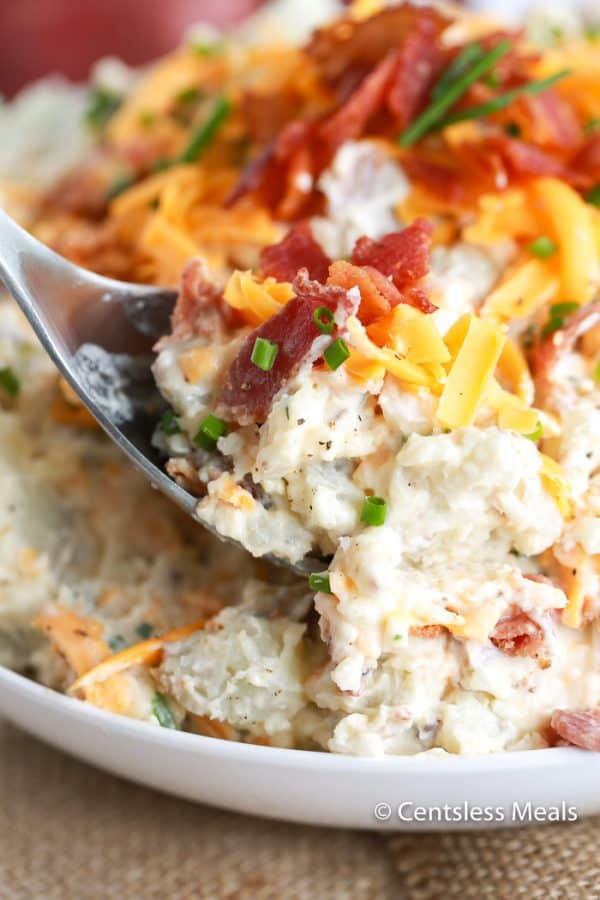 Loaded potato salad in a bowl with a scoop being taken out