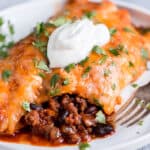 Beef enchiladas on a white plate with a dollop of sour cream