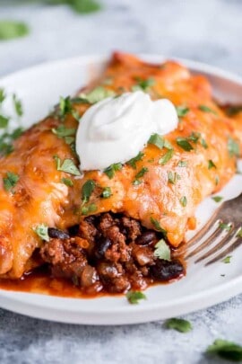 Beef enchiladas on a white plate with a dollop of sour cream
