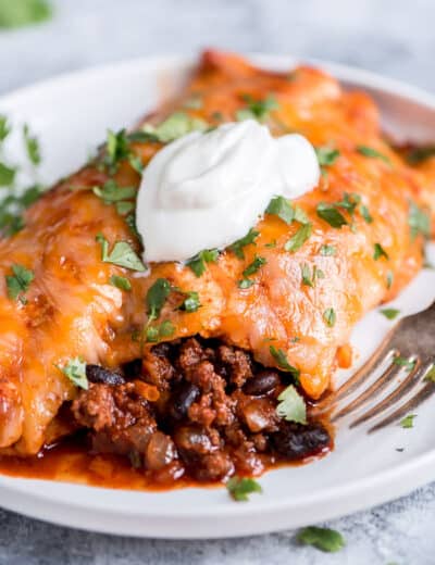 Beef enchiladas on a white plate with a dollop of sour cream