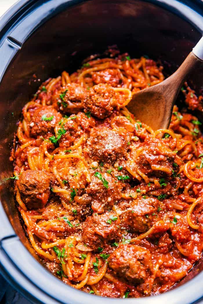 spaghetti and meatballs in a crock pot mixed with red sauce, parmesan cheese, and topped with parsley