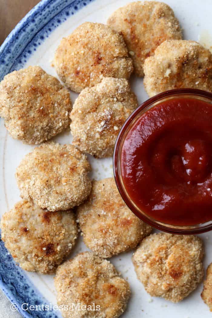 Homemade chicken nuggets on a plate with a bowl of ketchup