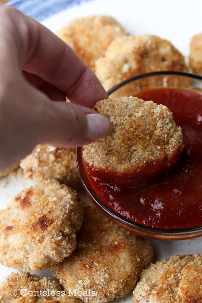 Homemade chicken nuggets with one being dipped in ketchup
