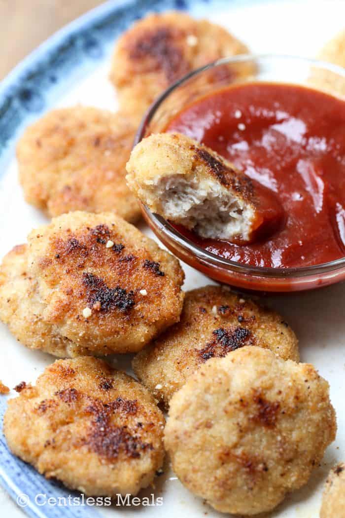 Homemade chicken nuggets with a bite taken out of one dipped in ketchup