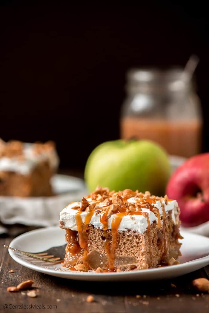 Caramel apple poke cake on a white plate with apples in the background