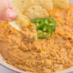 Chili cheese dip in a bowl with some being dipped onto a chip