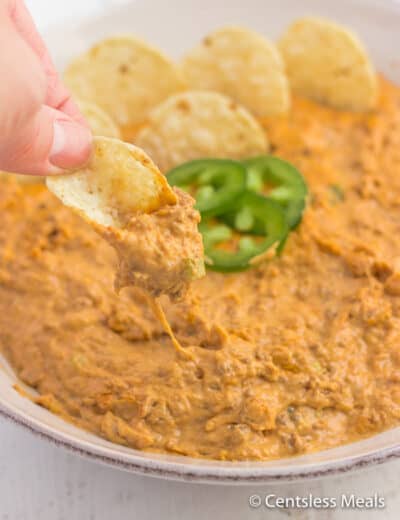 Chili cheese dip in a bowl with some being dipped onto a chip