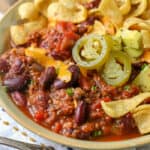 Crockpot chili in a bowl with jalapenos corn chips and cheddar cheese on top