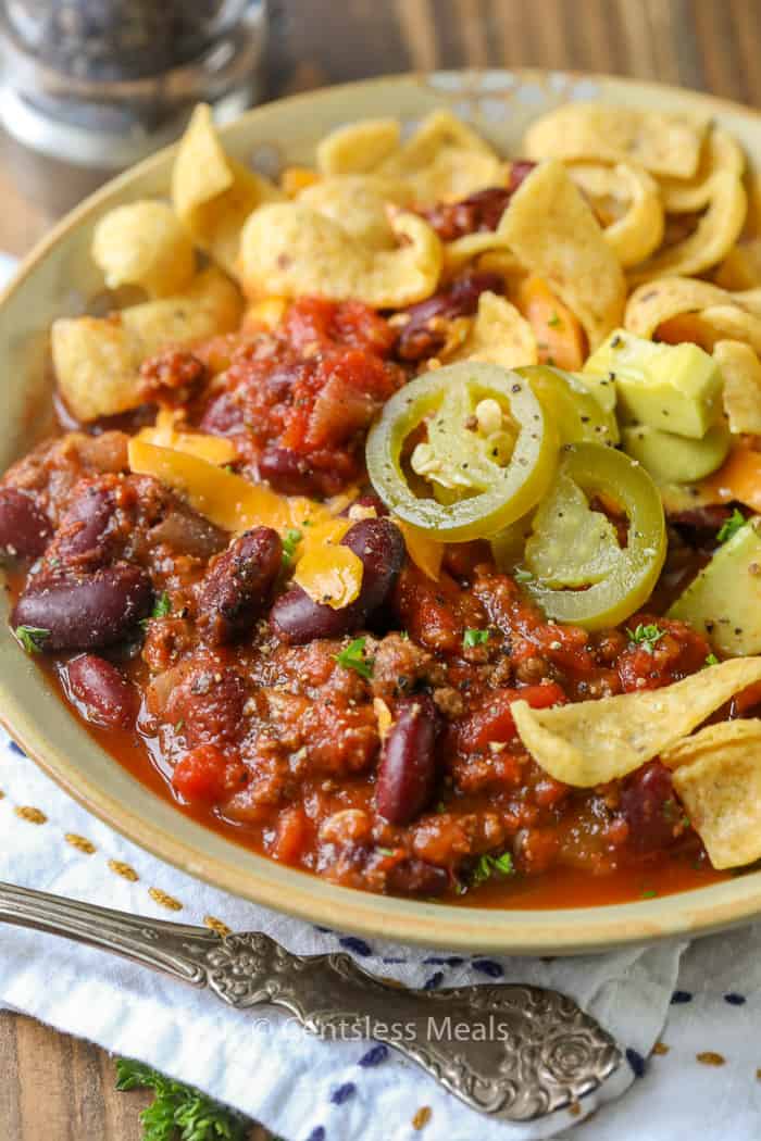 Crockpot chili in a bowl with jalapenos corn chips and cheddar cheese on top