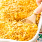 Funeral potatoes in a white casserole dish with a scoop being taken out
