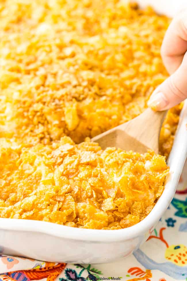Funeral potatoes in a white casserole dish with a scoop being taken out