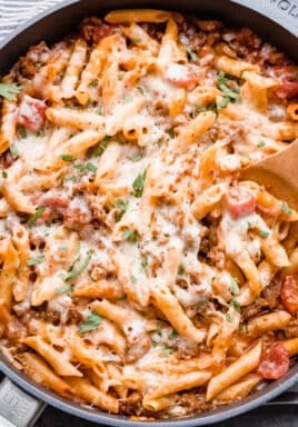 Italian sausage pasta in a skillet being dished out with wooden spoon.