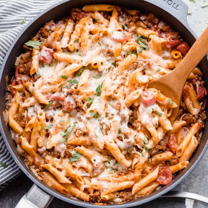 Italian sausage pasta in a skillet being dished out with wooden spoon.