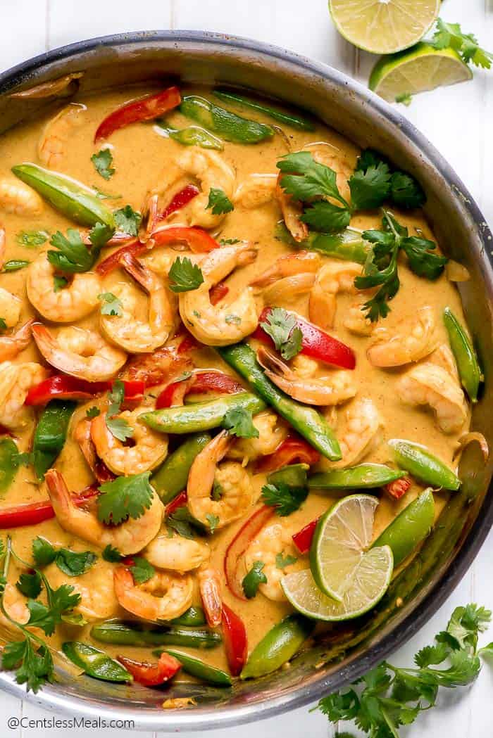 Shrimp curry in a pan with cilantro and lime wedges on the side