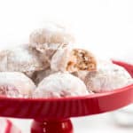 Snowball cookies on a red plate with a bite taken out of 1