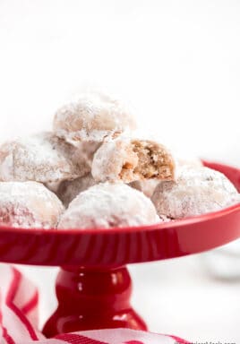 Snowball cookies on a red plate with a bite taken out of 1