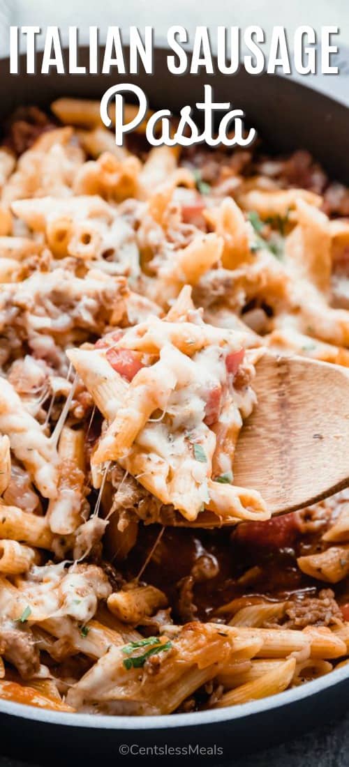 Italian sausage pasta in a pan with a wooden spoon and a title