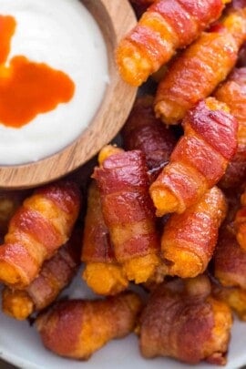 Bacon wrapped tater tots on a plate with a bowl of dip