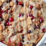 Cranberry bread pudding in a white casserole dish drizzled with sauce