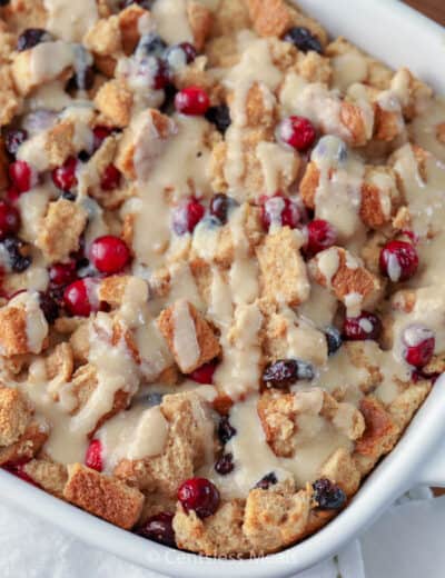 Cranberry bread pudding in a white casserole dish drizzled with sauce