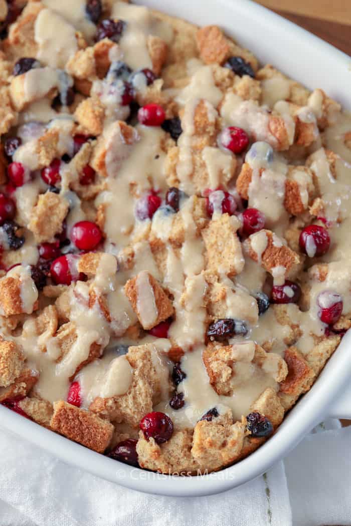 Cranberry bread pudding in a white casserole dish drizzled with sauce