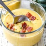 closeup of Squash Soup in a glass bowl with bacon garnish and a spoon