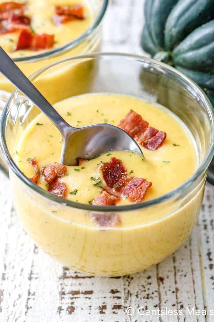 closeup of Squash Soup in a glass bowl with bacon garnish and a spoon