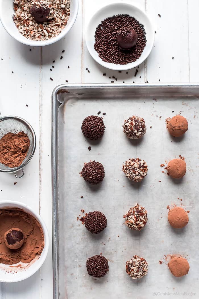 Chocolate truffles on a baking sheet and being dipped into sprinkles cocoa and nuts